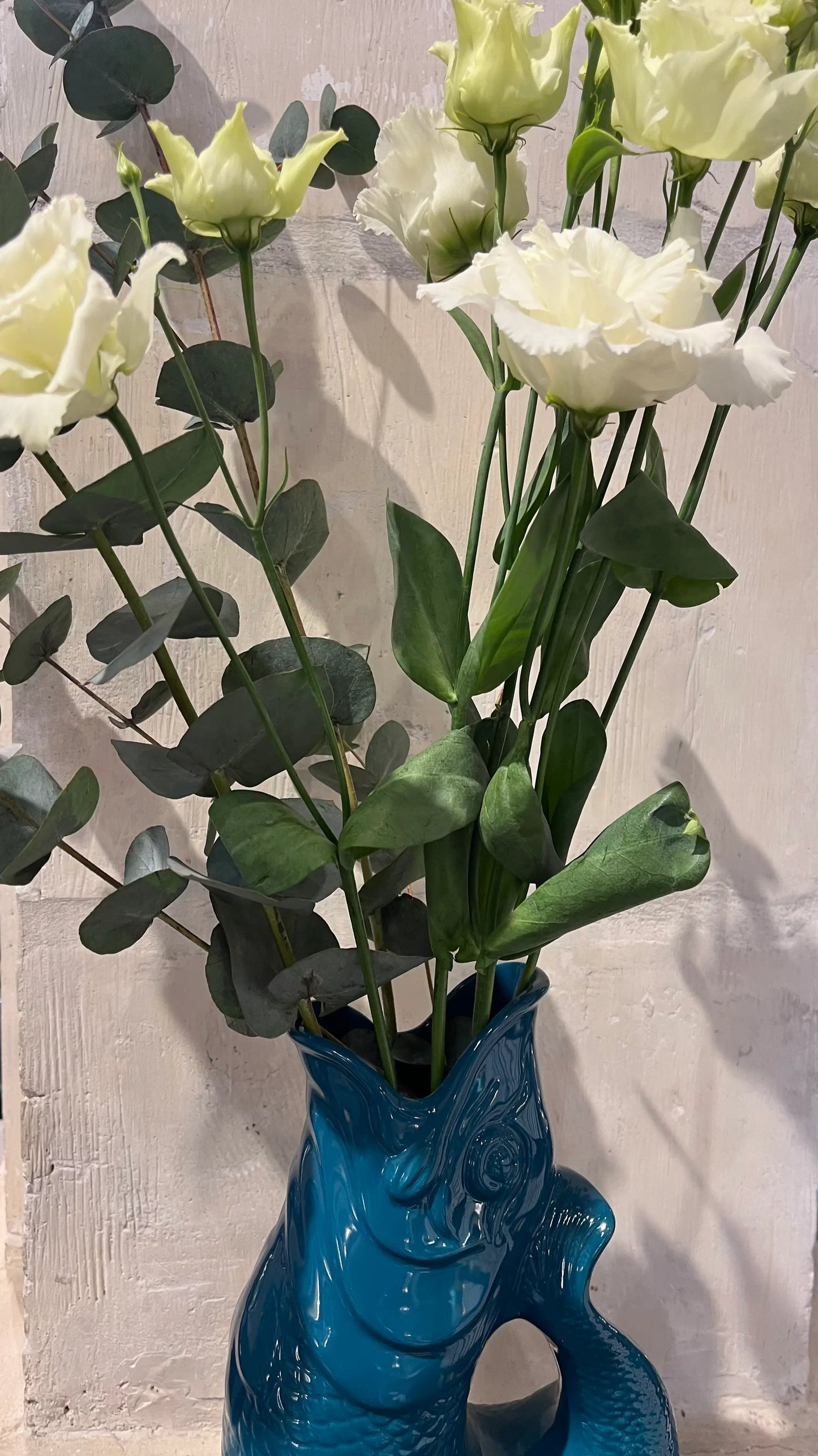 Vase Glouglou bleue pétrole fleuri devant un mur en pierre