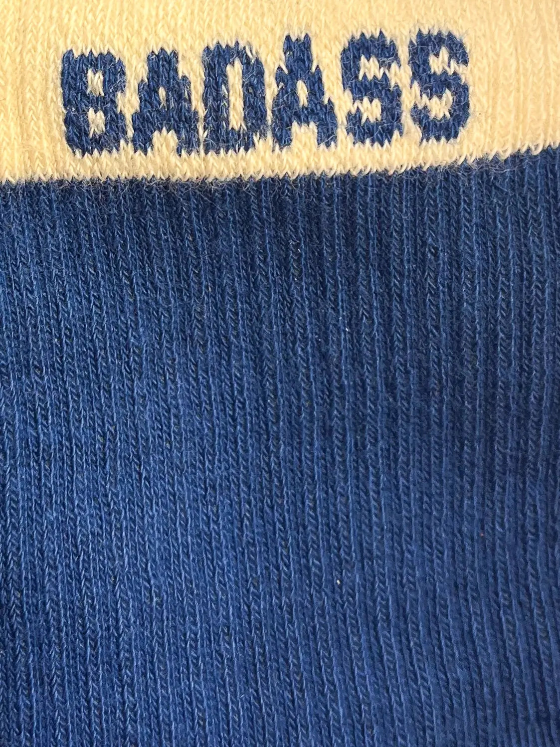 Focus sur la chaussette Félicie cousue en coton, bleue et blanche avec « Badass» écris en bleu