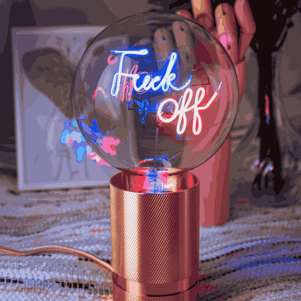Ampoule Message in the bulb avec l'expression Fuck Off dans un style manuscrit qui s'illumine en bleu pour Fuck et en rouge pour Off - présentation Lifestyle devant une main en bois