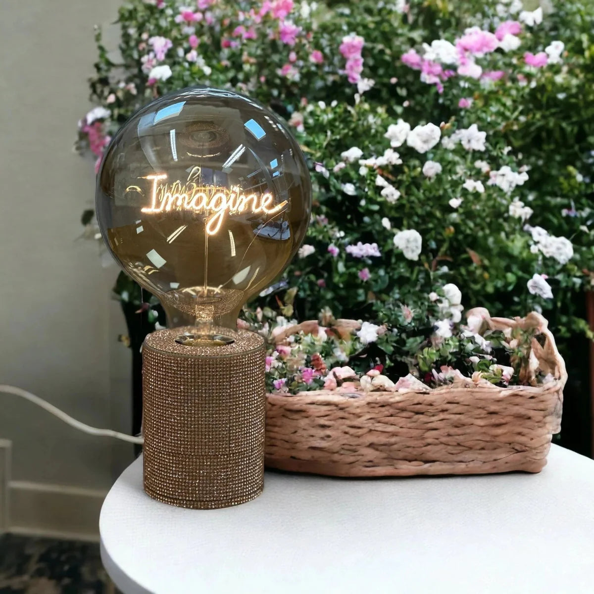 Ampoule à message Imagine Message in the Bulb présenté sur socle à paillettes devant des fleurs