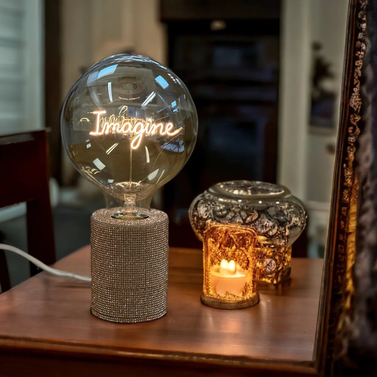 Ampoule à message Imagine Message in the Bulb présenté sur socle à paillettes devant un miroir