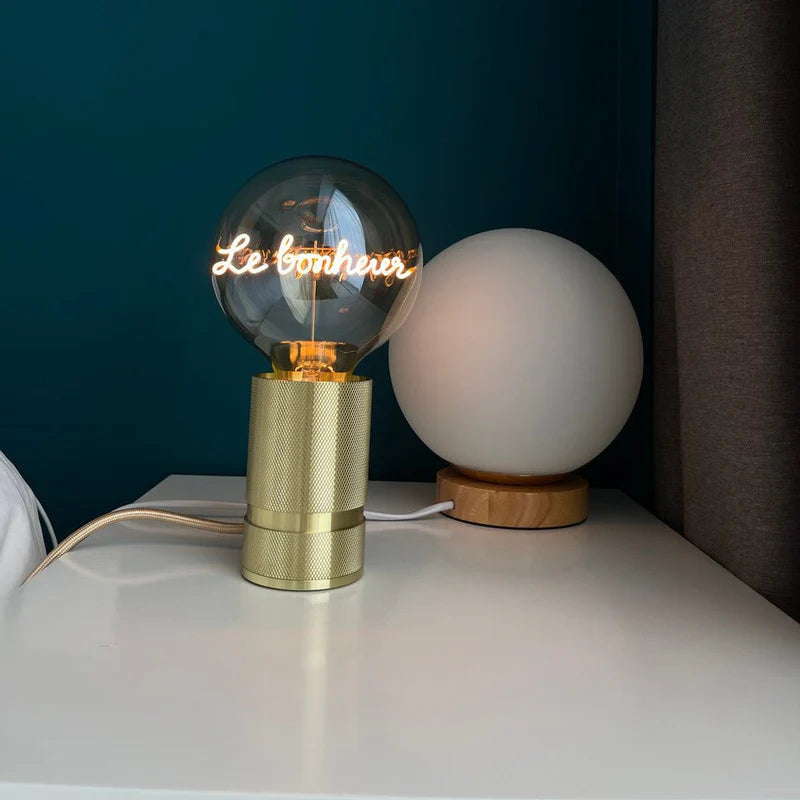 Ampoule Message in the Bulb verre ambré message Le Bonheur sur socle doré sur table blanche
