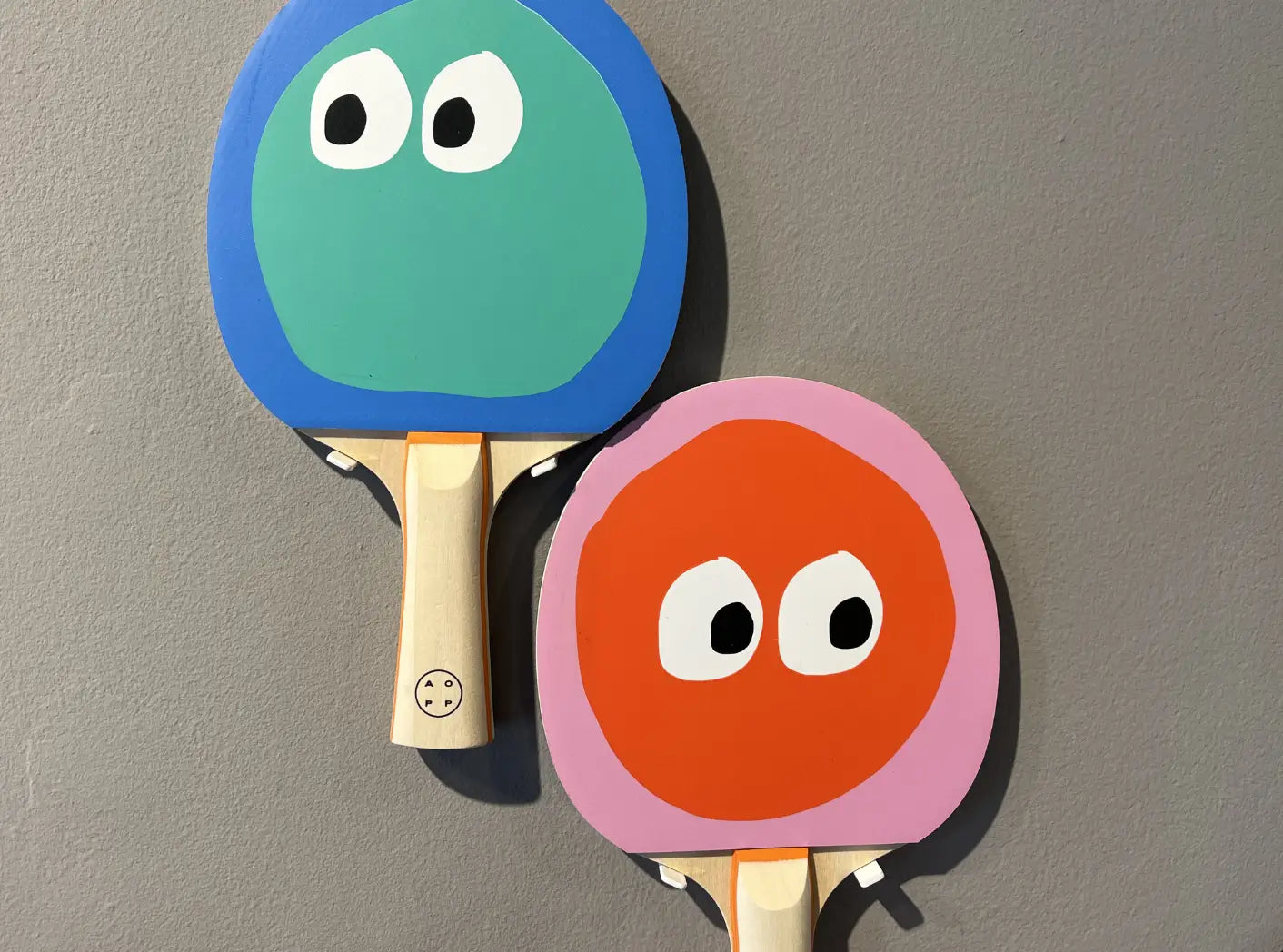Raquettes de ping-pong Art of Ping Pong Face Off montrant leurs deux faces colorées : bleu et vert d'un côté, rose et rouge de l'autre.