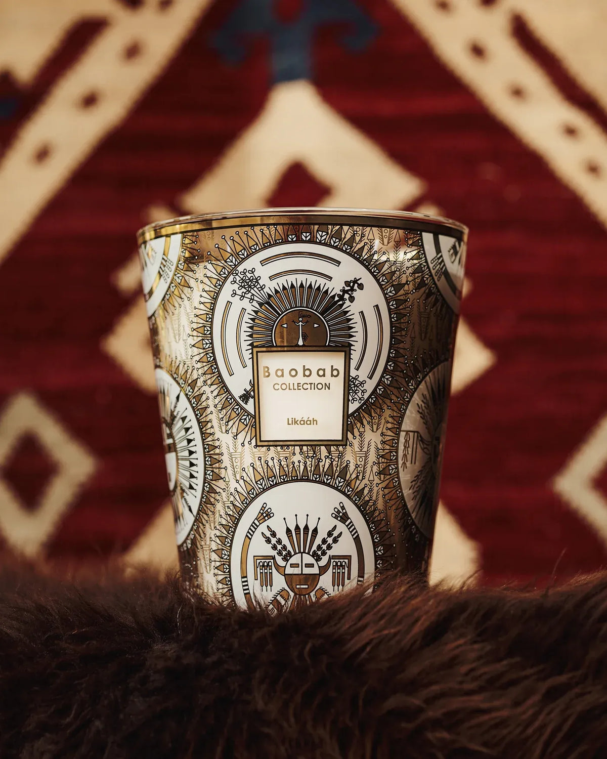 Bougie Likááh Baobab Collection avec décor géométrique noir et or devant un textile à motifs graphiques