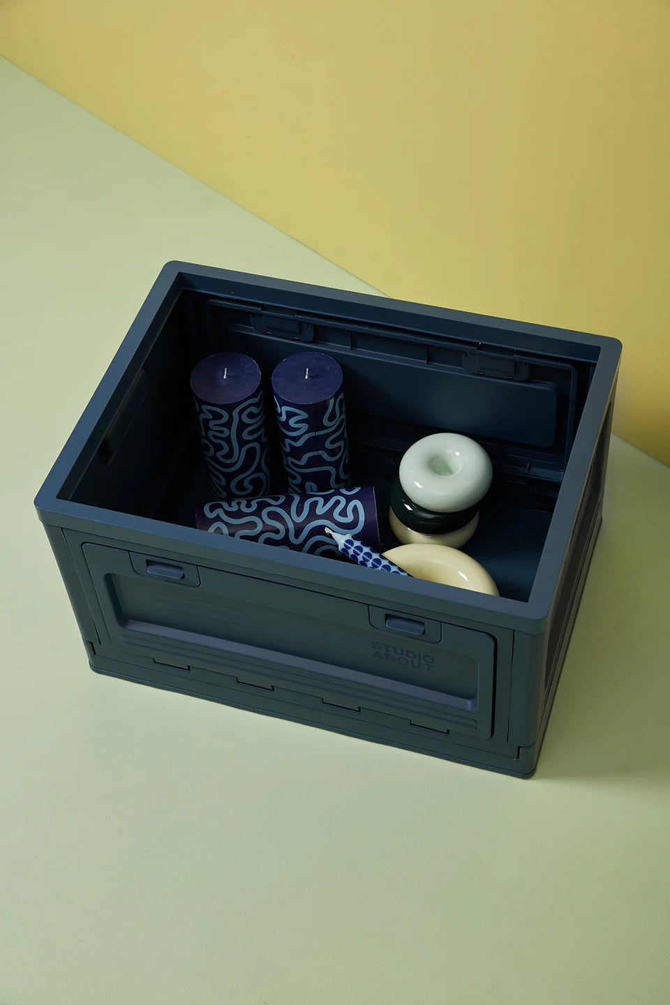 Boite Studio About bleu foncé ouverte sur le dessus avec à l'intérieur des bougies piliers et des bougeoirs de la même marque.