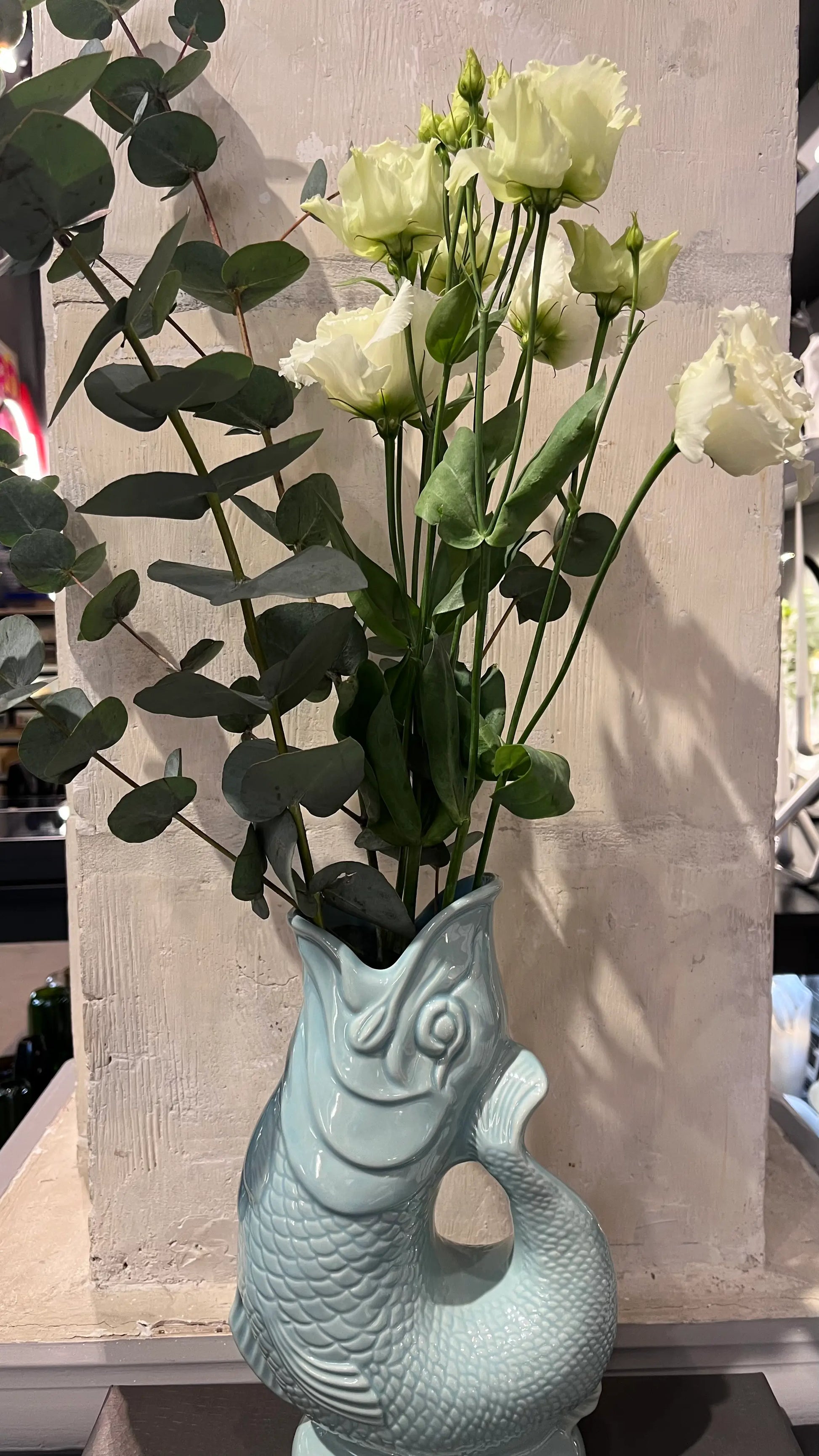 Vase Glouglou eau de Nil avec des fleurs, devant un pilier en pierre 