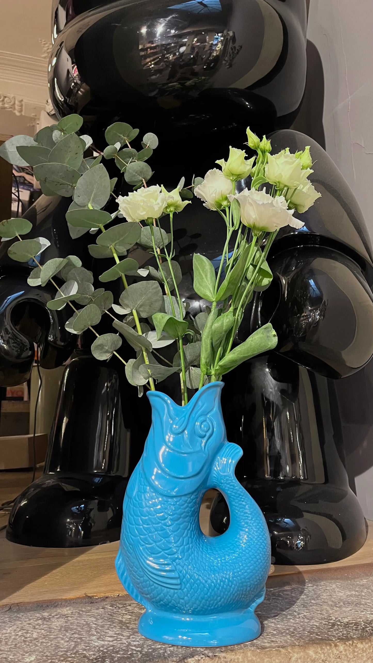 Vase Glouglou turquoise avec des fleurs, devant une statue de lapin noir