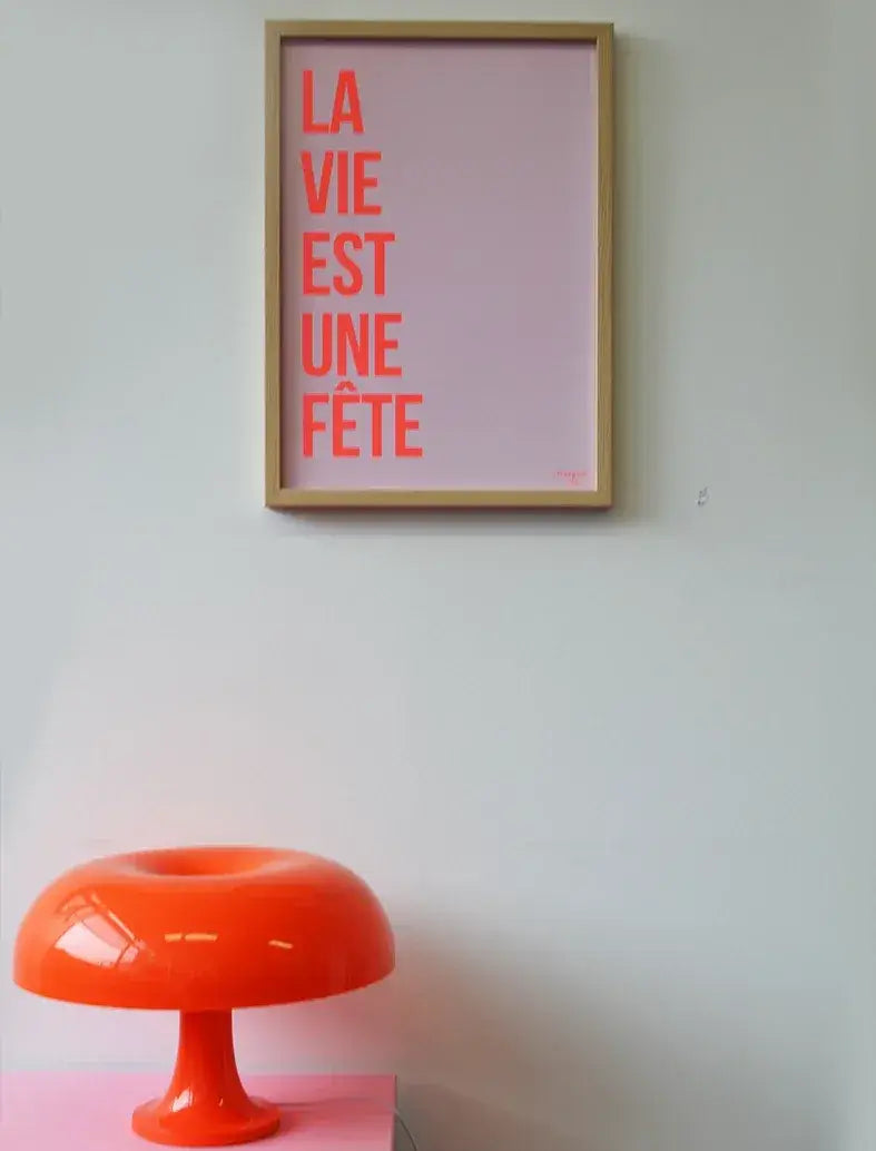Affiche "La vie est une fête" encadrée en orange fluo sur fond rose.