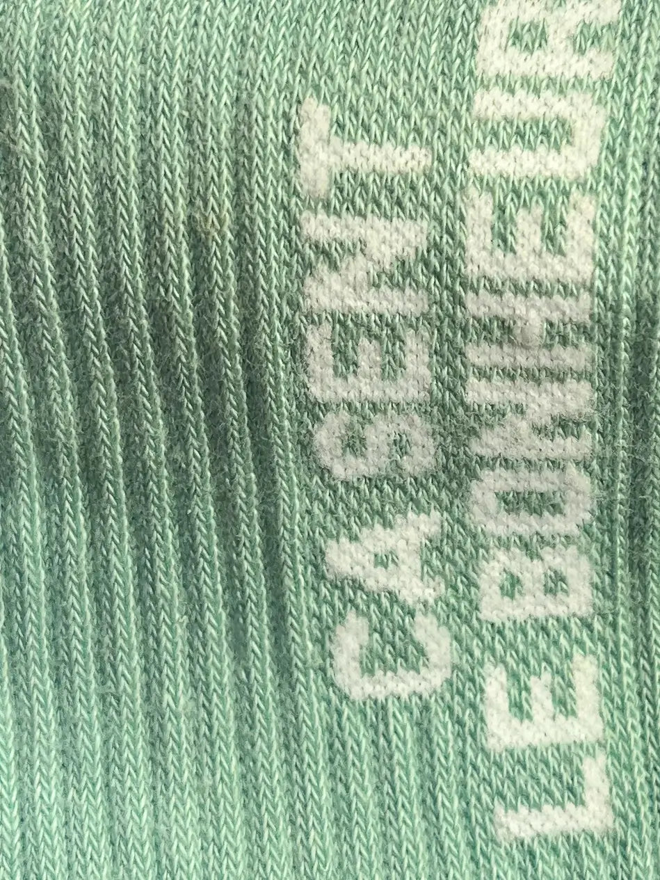 Focus sur la chaussette Félicie cousue en coton, turquoise avec « ça sent le bonheur » écris en blanc