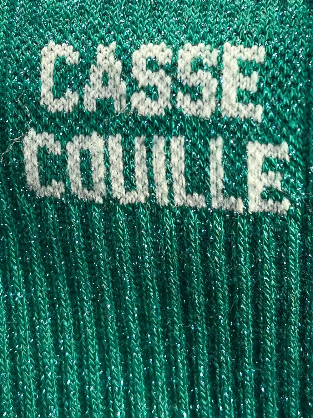 Focus sur la chaussette Félicie cousue en coton, verte à paillettes avec « casse couille » écris en blanc