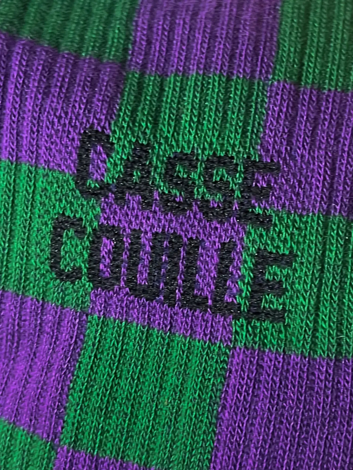 Focus sur la chaussette Félicie cousue en coton, damier vert et violet avec « casse couille » écrit en noir