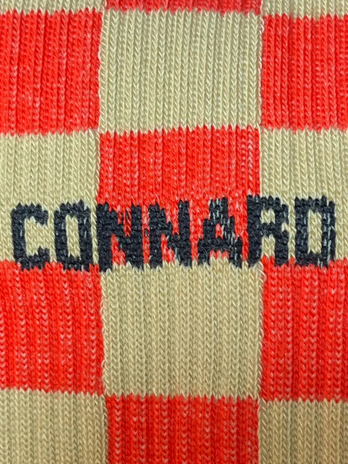 Focus sur la chaussette Félicie cousue en coton, damier sable et orange avec « connard » écrit en noir