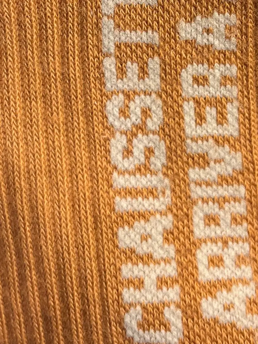 Focus sur la chaussette Félicie cousue en coton, beige avec « chaussette pour arriver à l'heure  » écris en blanc