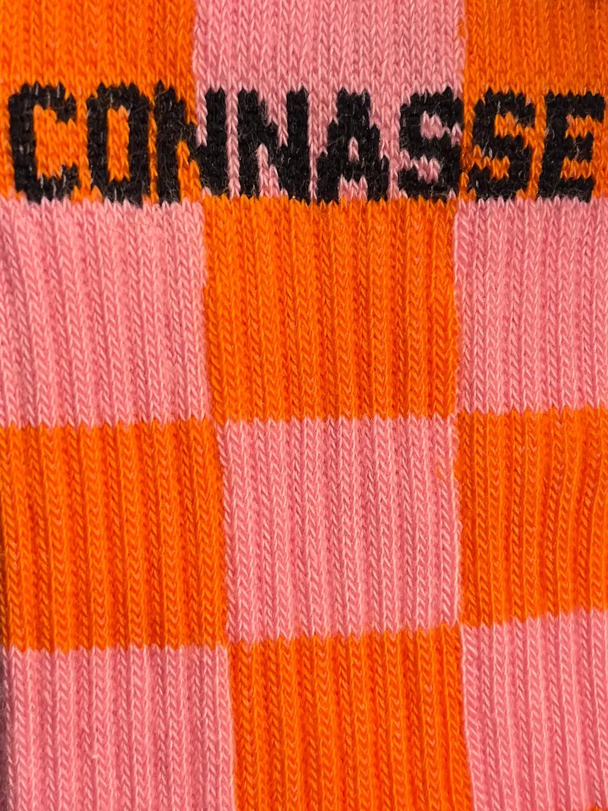 Focus sur la chaussette Félicie cousue en coton, motif en damier rose et orange avec « connasse » écris en noir