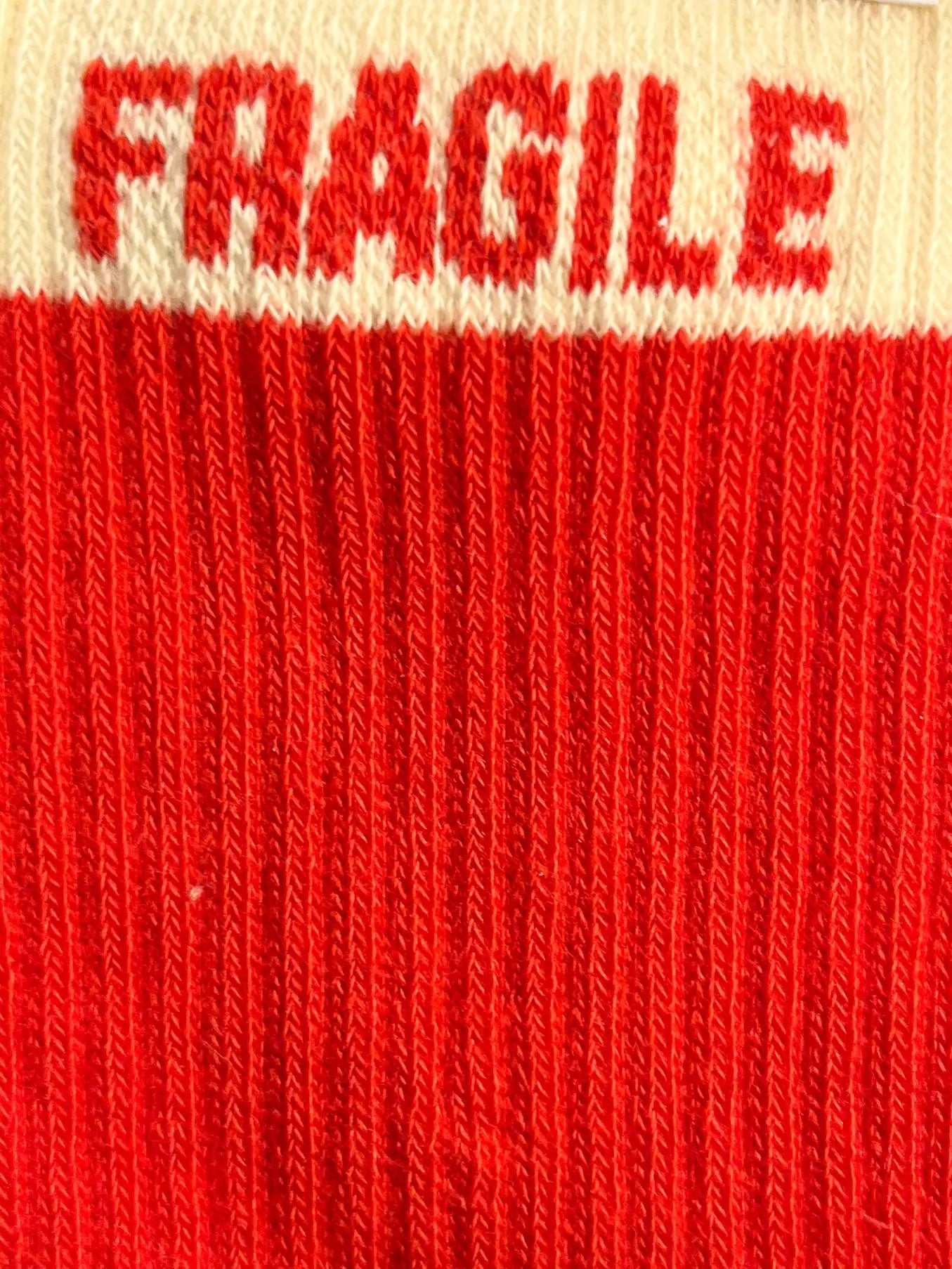 Focus sur la chaussette Félicie cousue en coton, couleur rouge et blanche avec « Fragile » écris en rouge