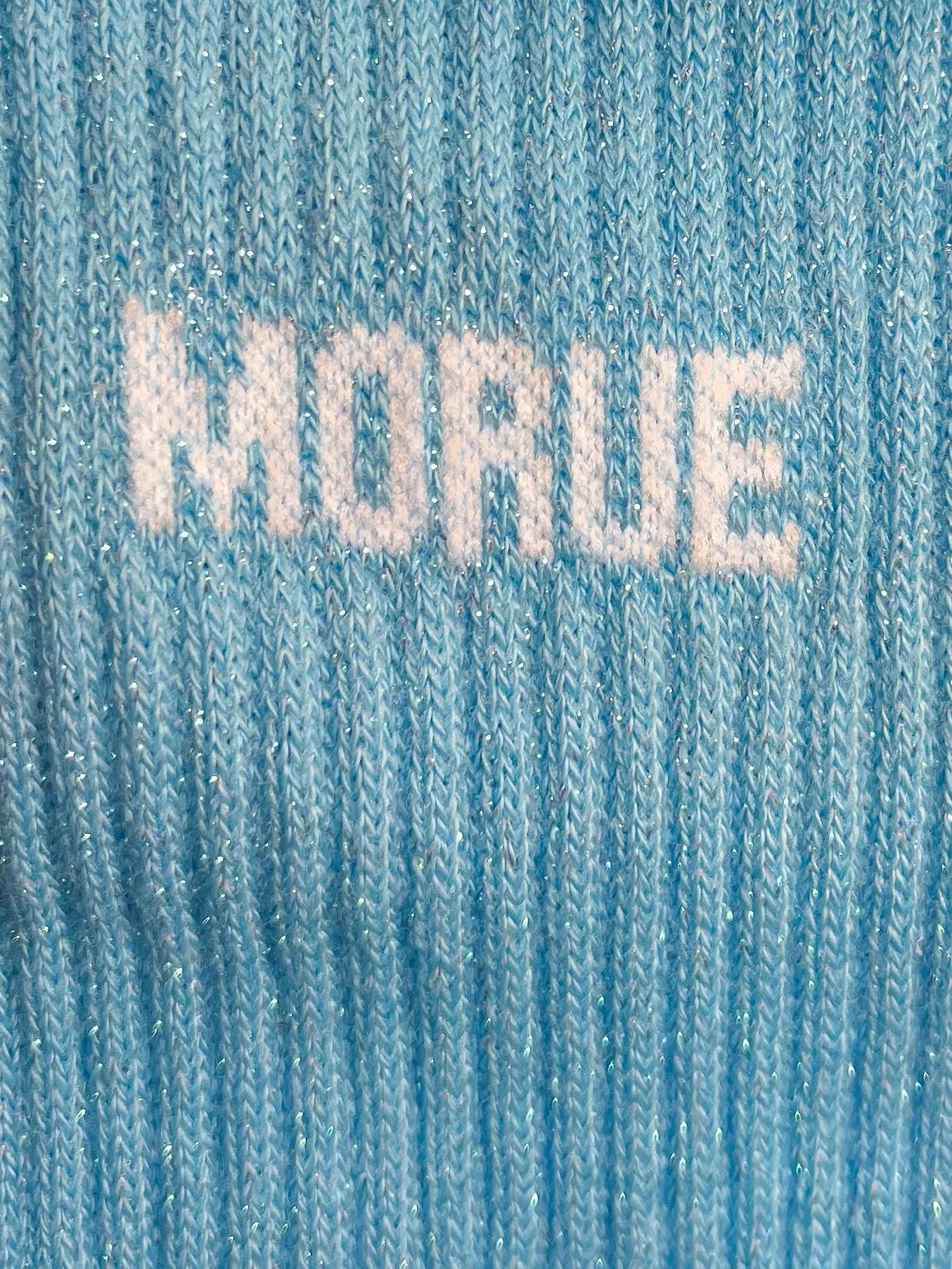 Focus sur la chaussette Félicie cousue en coton, bleue ciel à paillettes avec « Morue » écris en blanc