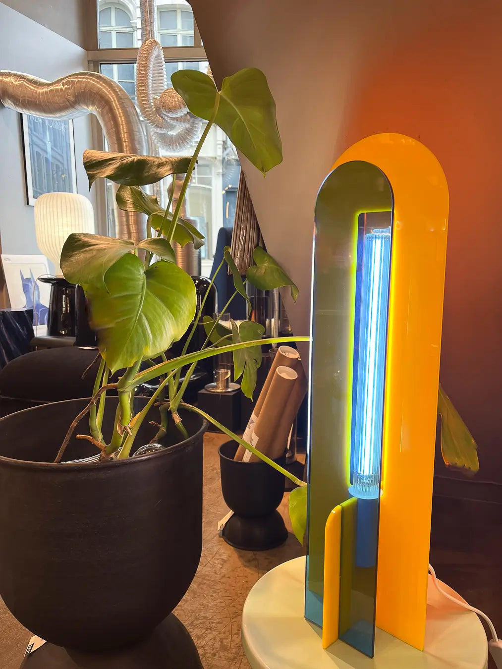 Lampe Andy jaune, bleu et orange allumée, à côté d'une plante