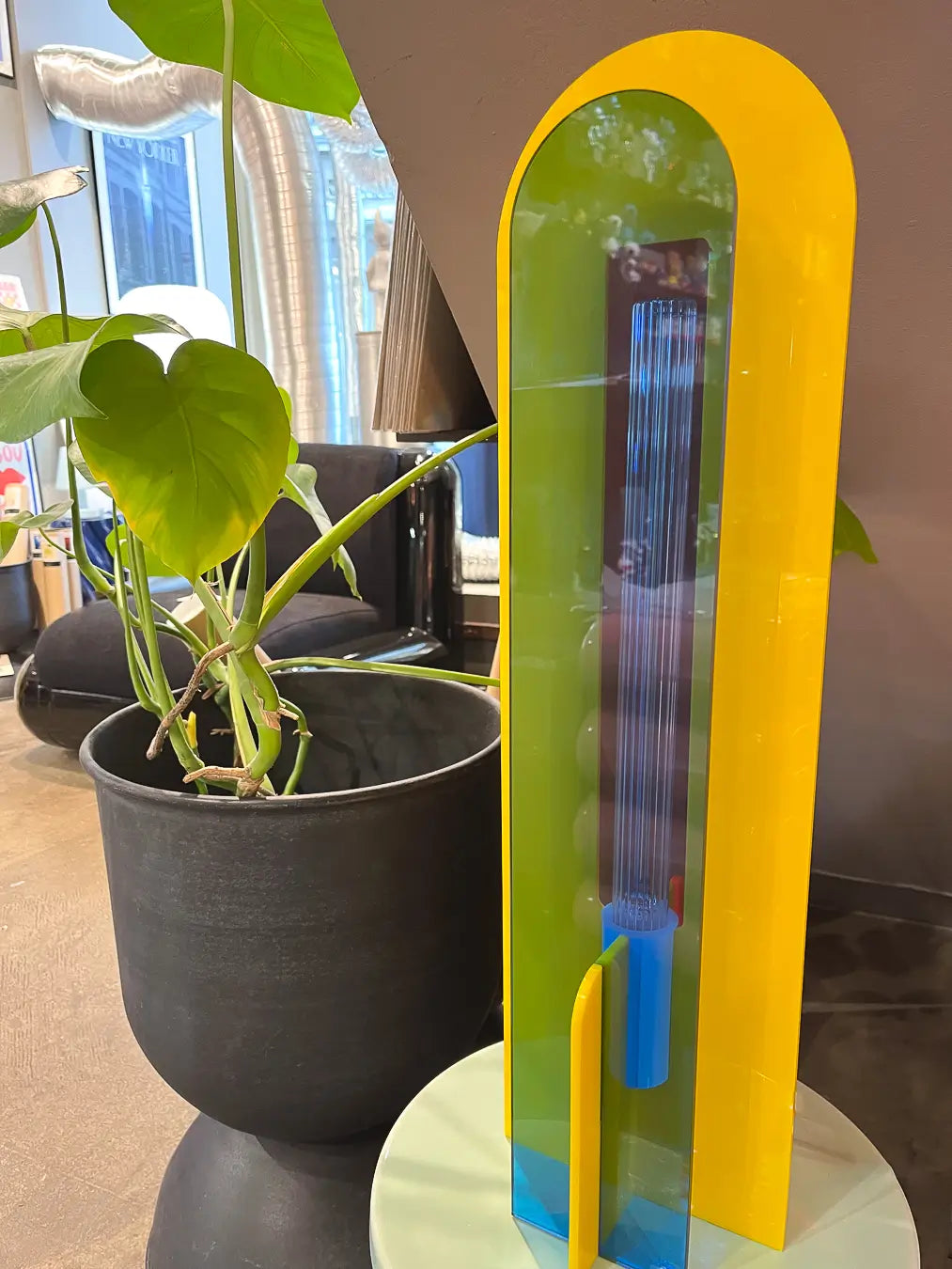 Lampe Andy jaune, bleu et orange éteinte, à côté d'une plante