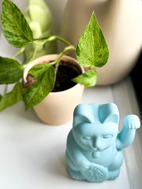 Maneki Neko bleu clair posé sur un rebord de fenêtre près d'une plante