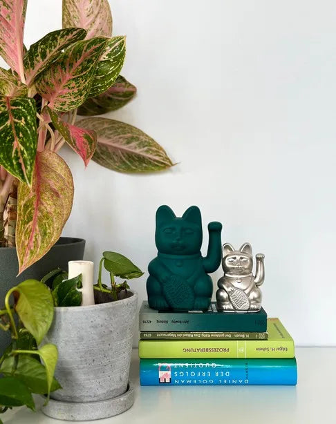 Maneki Neko vert posé sur une pile de livres près d'une plante