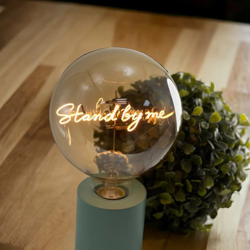 Ampoule MITB "Stand by me" sur une table à côté d'une plante