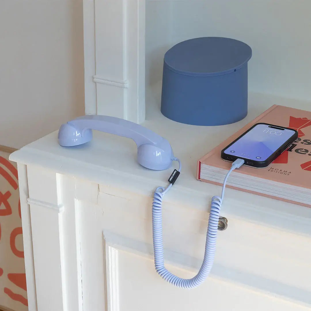 Combiné de téléphone Pop Phone Azur branché à un smartphone et posé sur une cheminée, pour rappeler les anciens téléphones fixes avec combiné