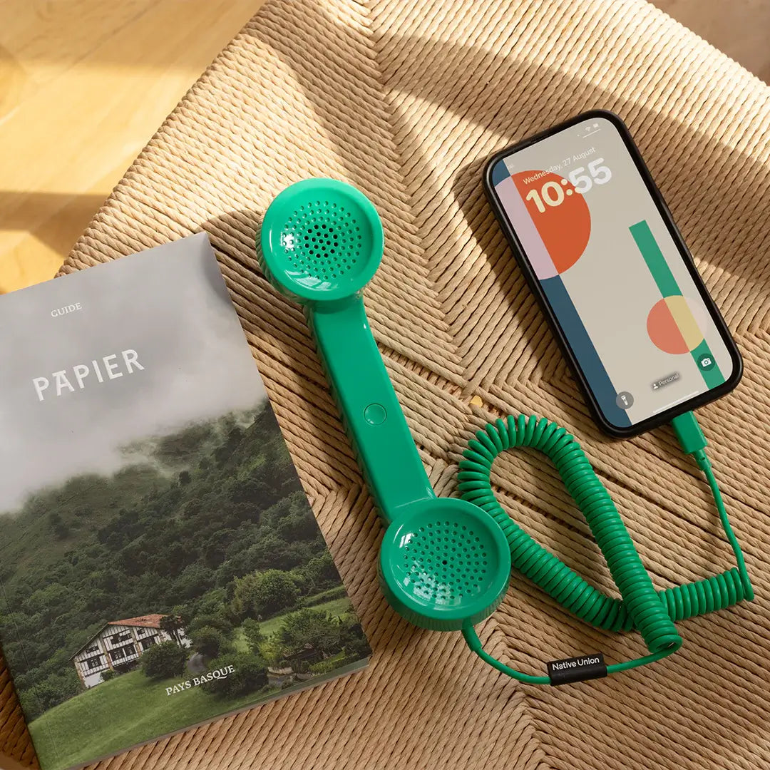 Combiné de téléphone Pop Phone Vert Pin de chez Native Union, branché à un smartphone avec un câble USB-C, dans un salon illuminé.