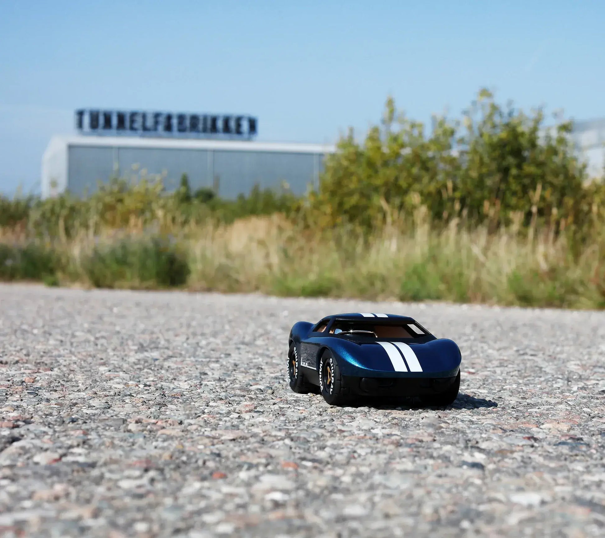 Voiture miniature Playforever Ken Cash bleu nuit et cuivre dans un environnement industriel