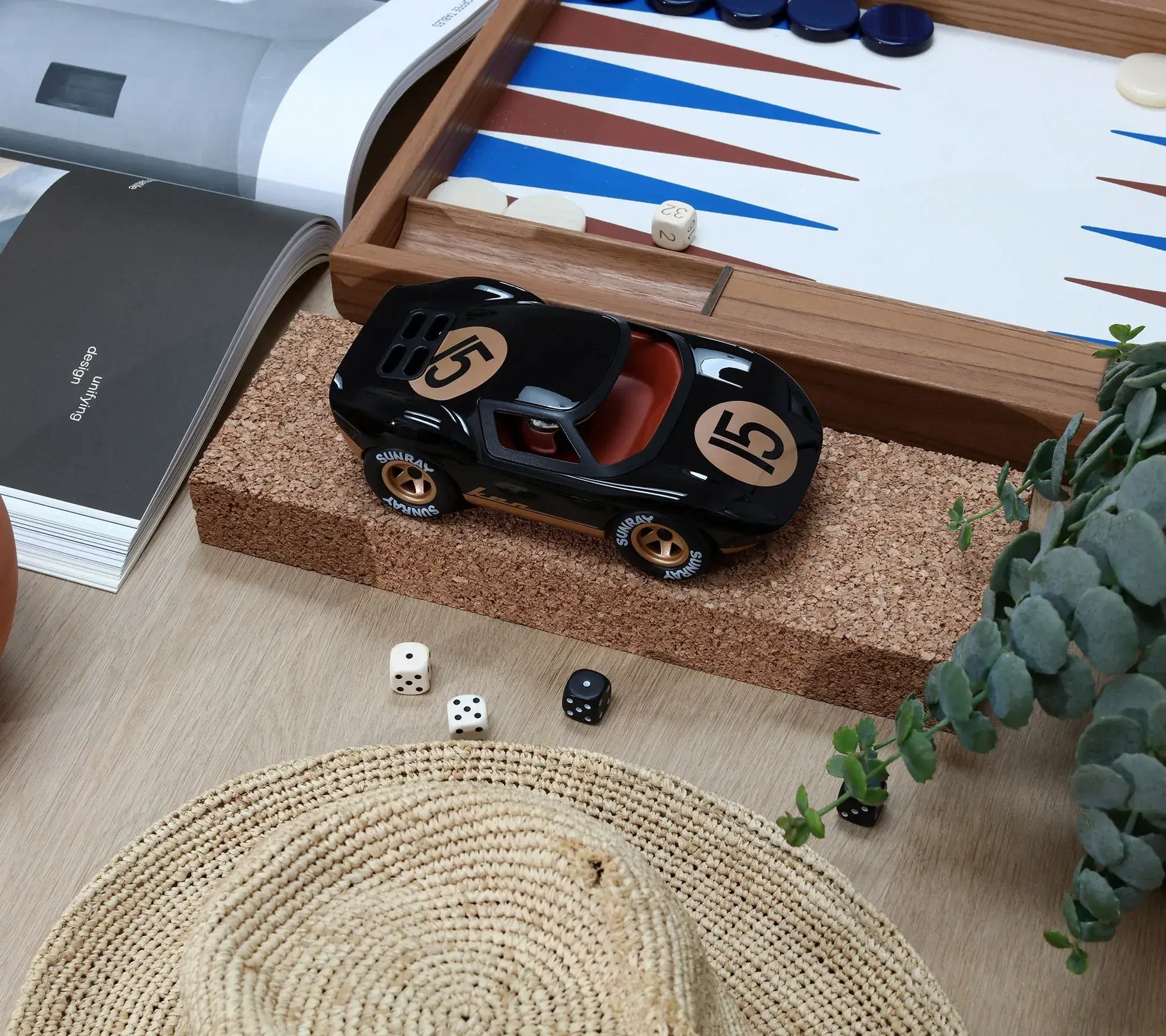 Voiture miniature Playforever Ken Cave noire et or sur une table avec jeu de backgammon