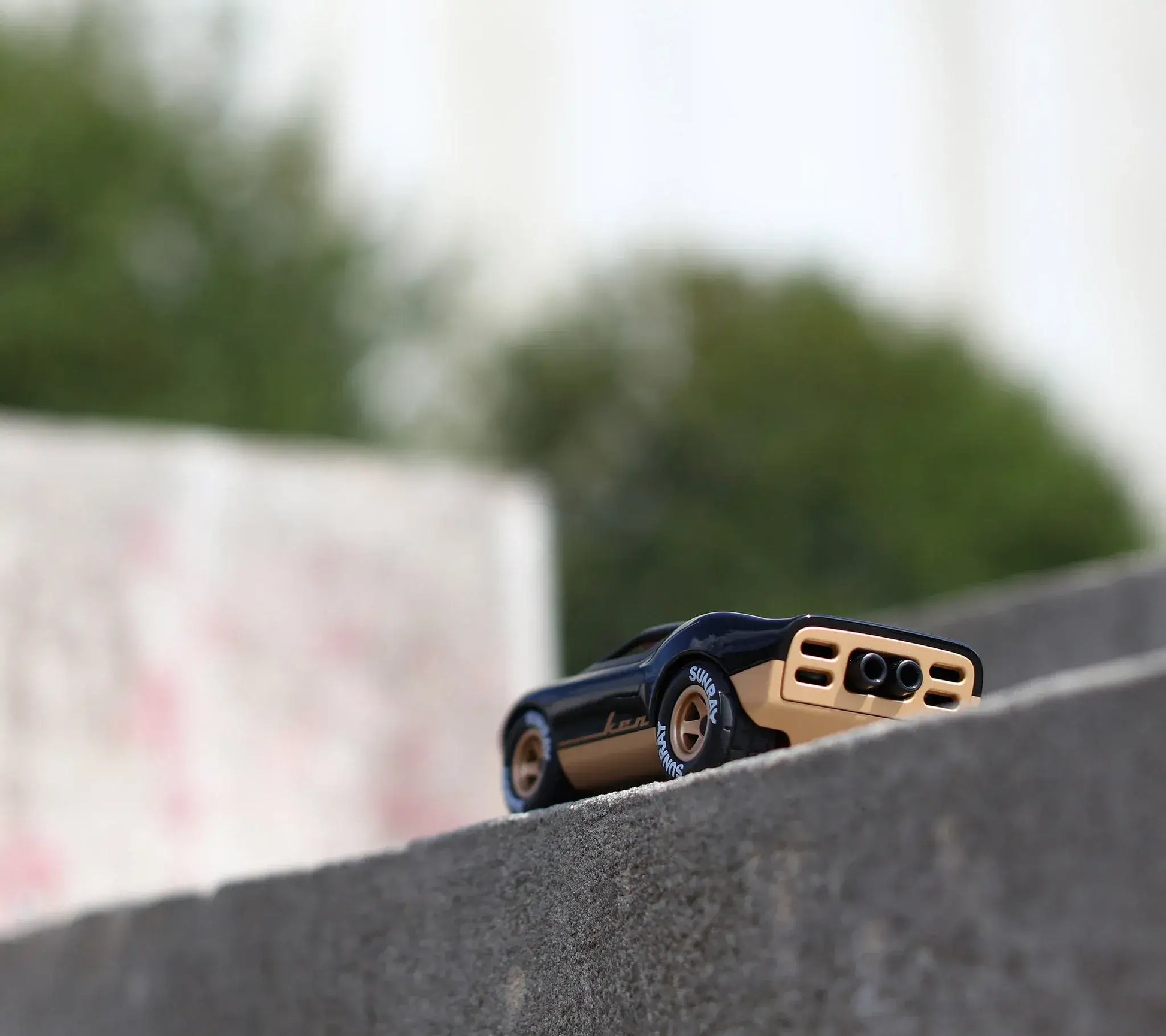 Voiture miniature Playforever Ken Cave noire et or posée vue arrière sur un muret en béton