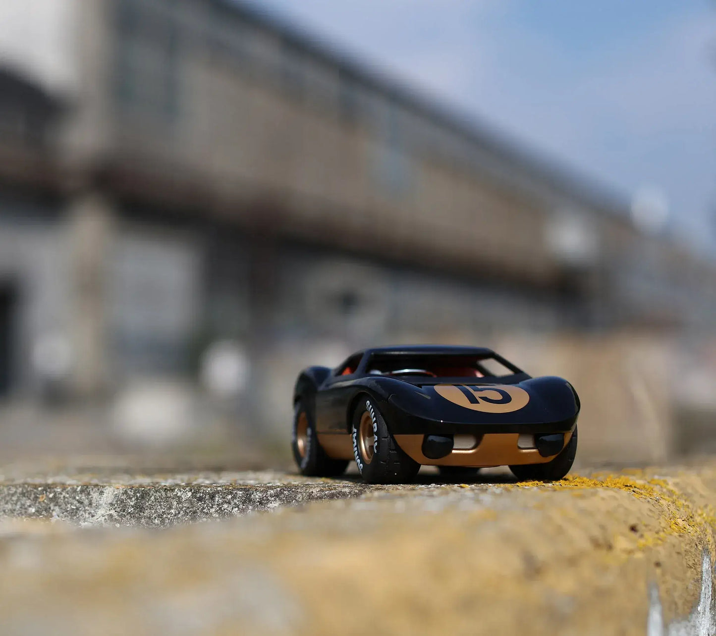 Voiture miniature Playforever Ken Cave noire et or vue trois quarts dans un décor industriel