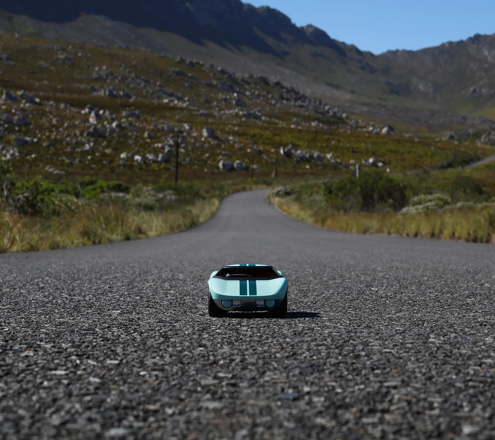 Voiture miniature Playforever Ken Parton turquoise vue de face sur une route de montagne