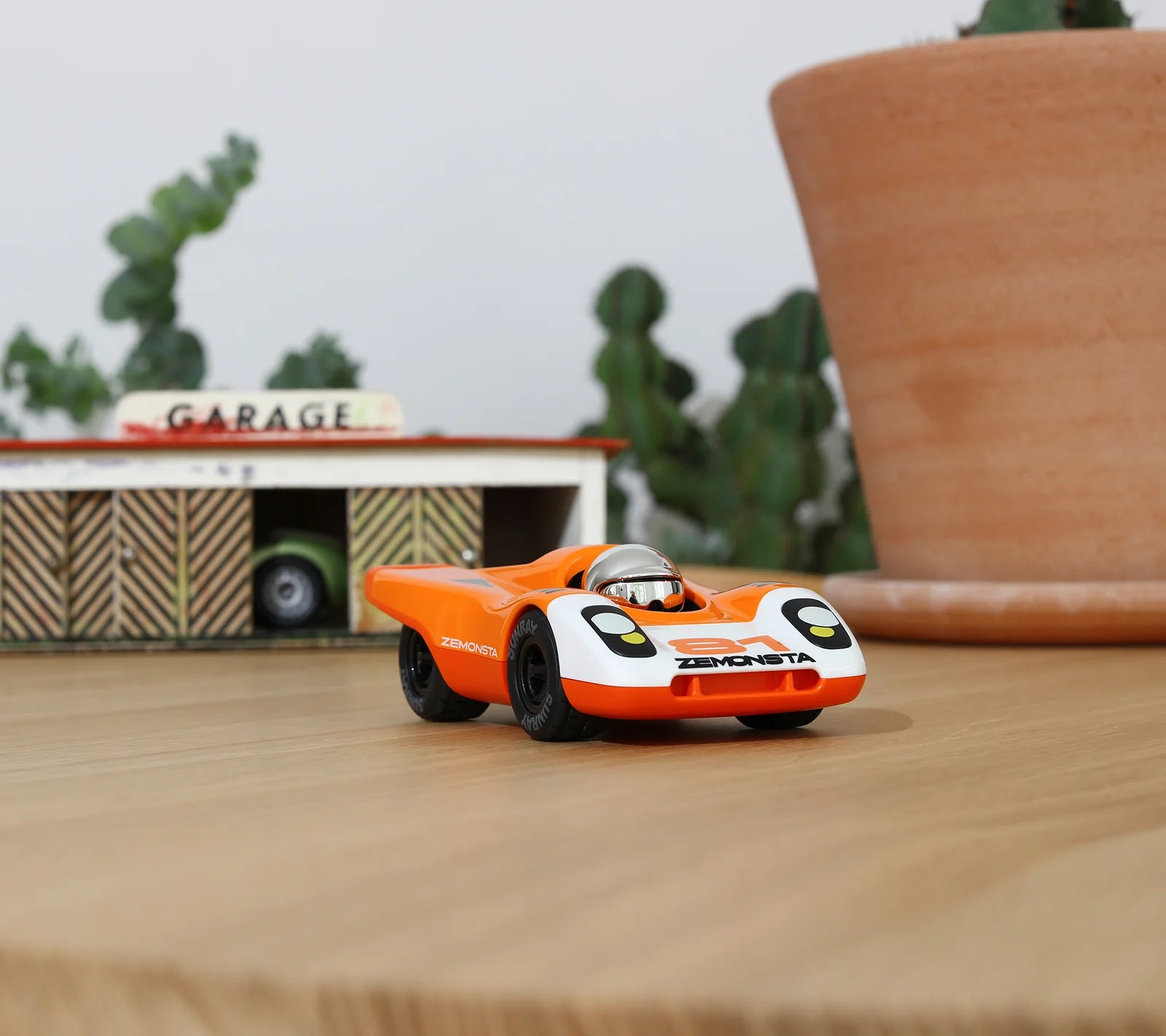 Voiture miniature orange Zemonsta Egon devant un garage miniature