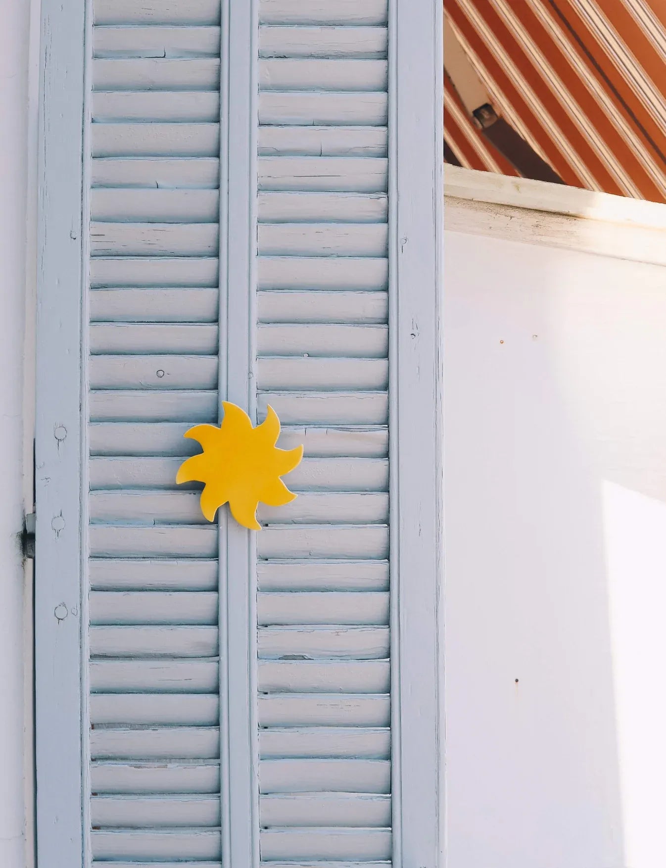 Soleil mural jaune en céramique émaillée sur des volets bleus