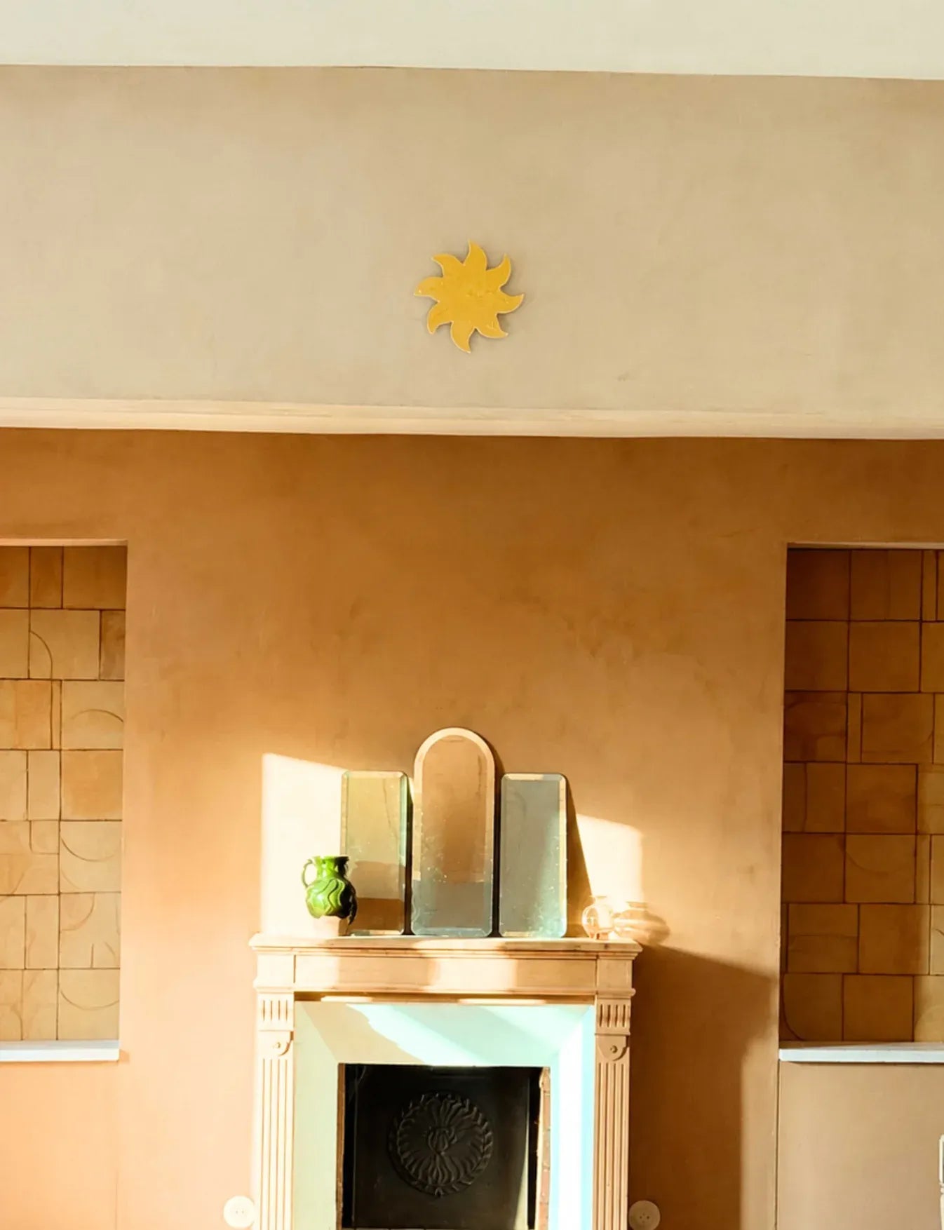 Soleil mural jaune en céramique émaillée au-dessus d’une cheminée