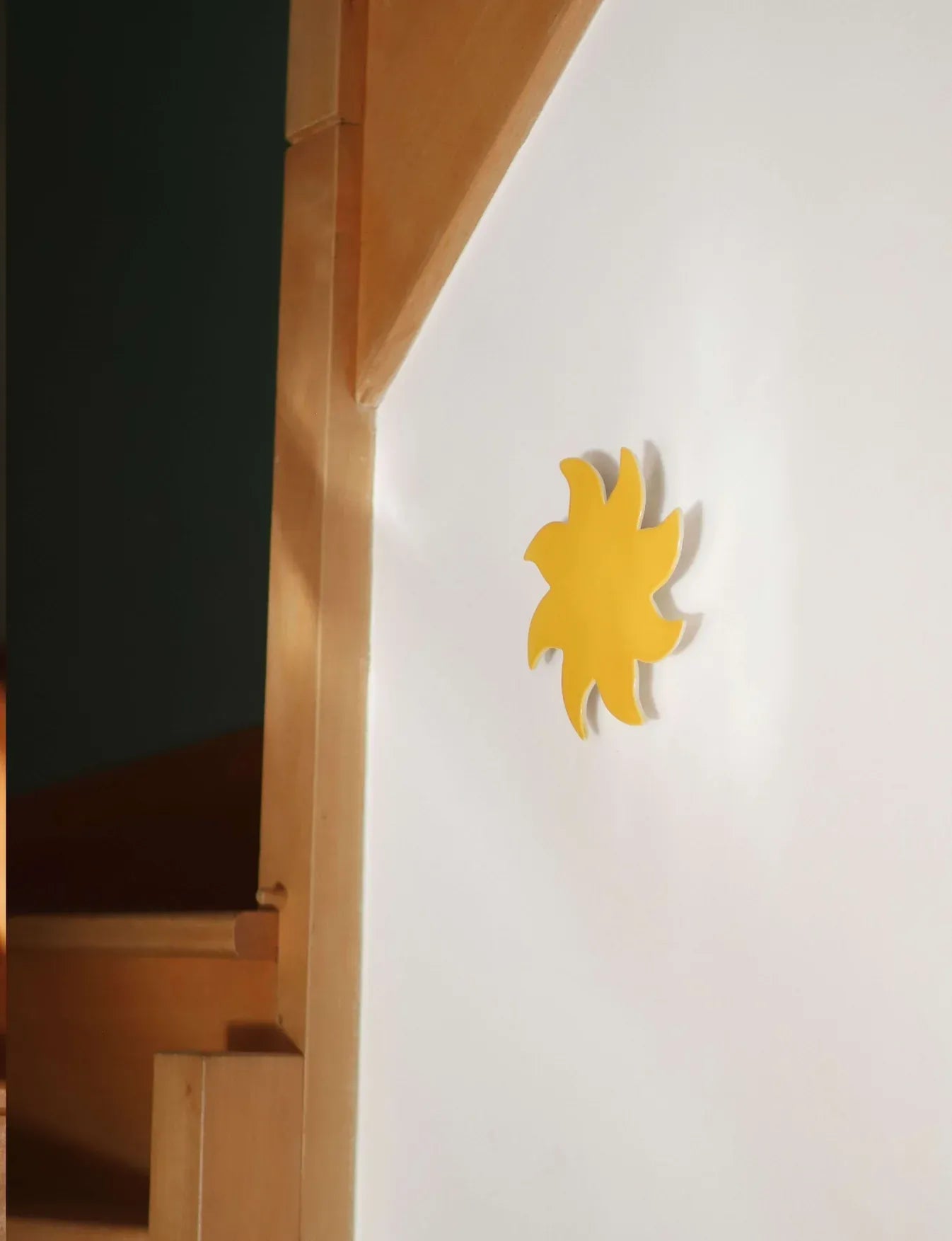 Soleil mural jaune en céramique émaillée avec ombre portée sur un mur blanc