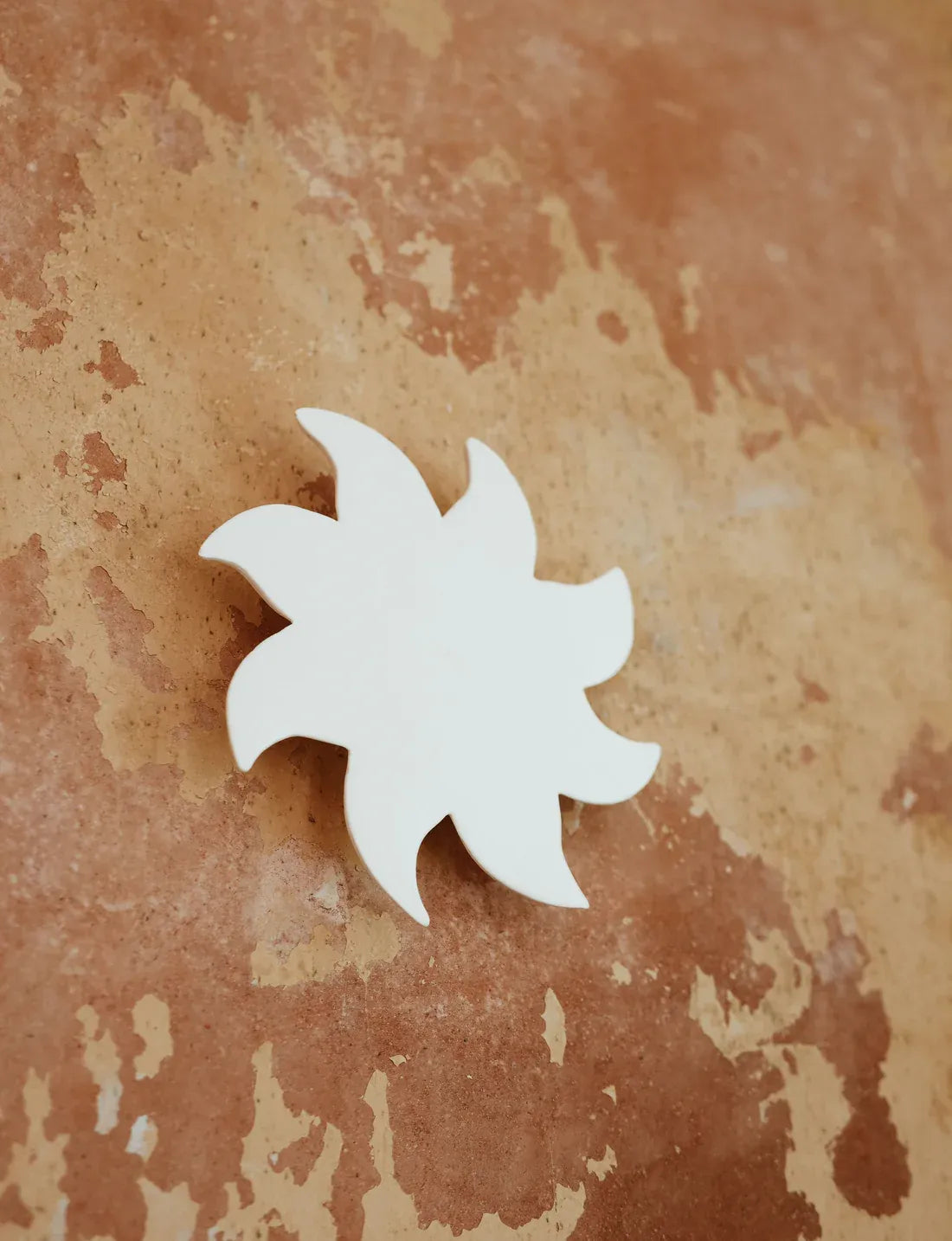 Soleil mural blanc en céramique sur un mur terracotta patiné