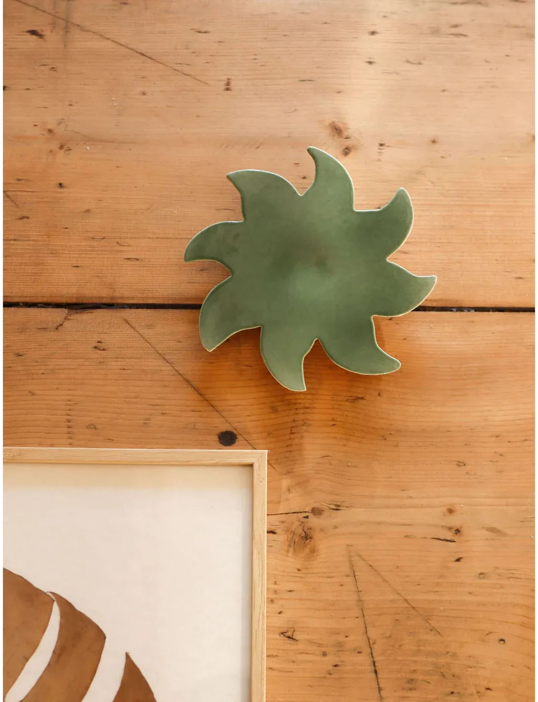 Soleil mural vert en céramique Maison Béata sur un mur en bois