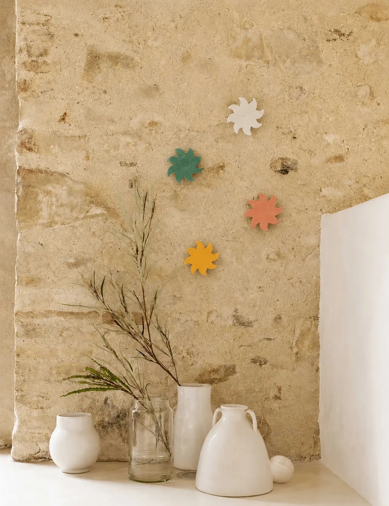 Composition de soleils muraux en céramique colorée Maison Béata sur un mur en pierre