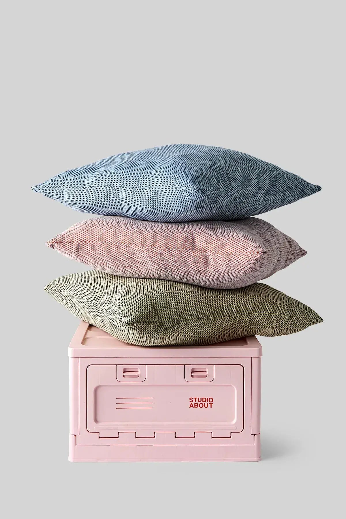 Boite de rangement rose avec les coussins rouge, bleu et jaune empilés dessus
