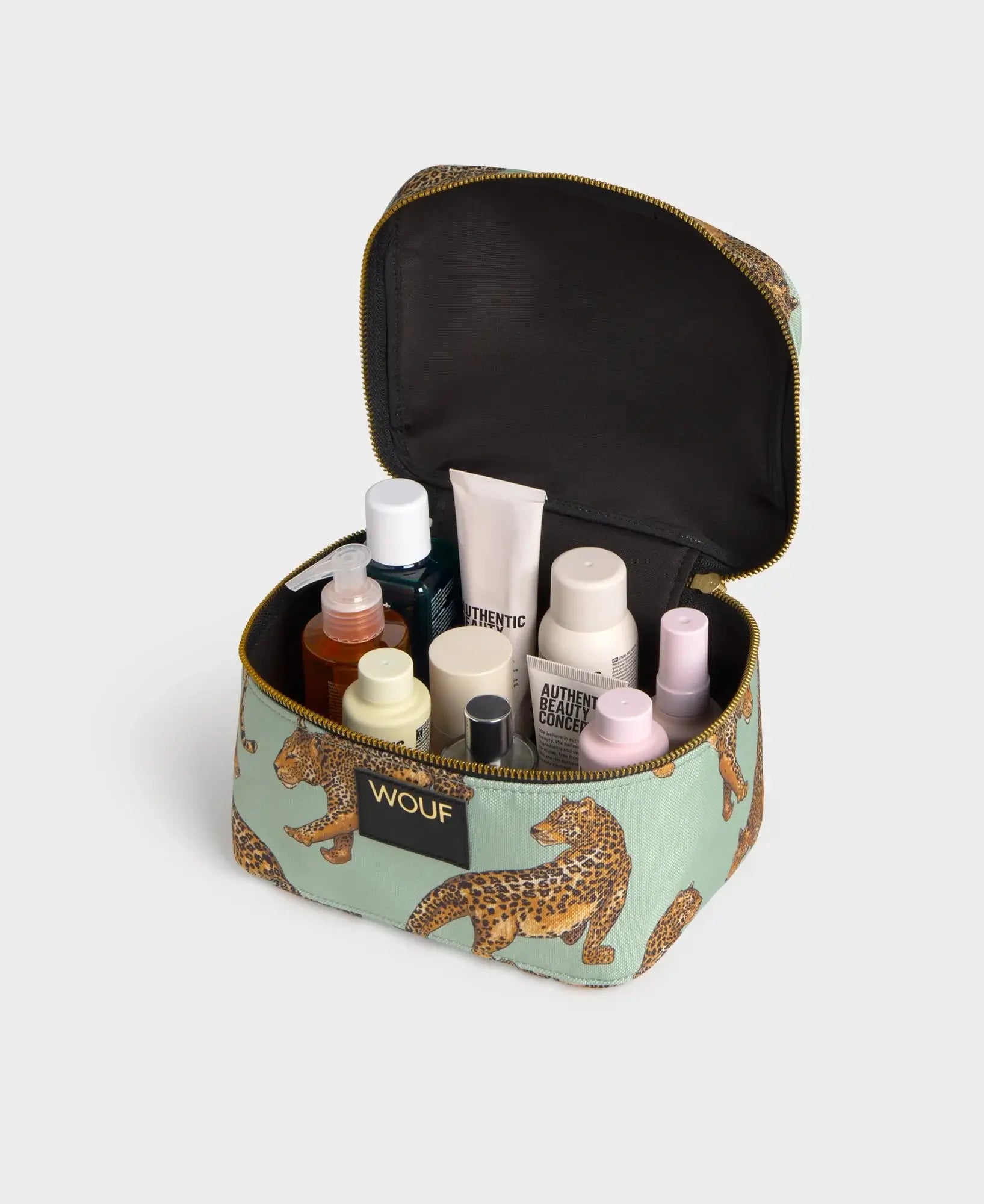 Trousse de toilette vanity Emerald Leopard de chez Wouf ouverte avec des produits de beauté et du maquillage
